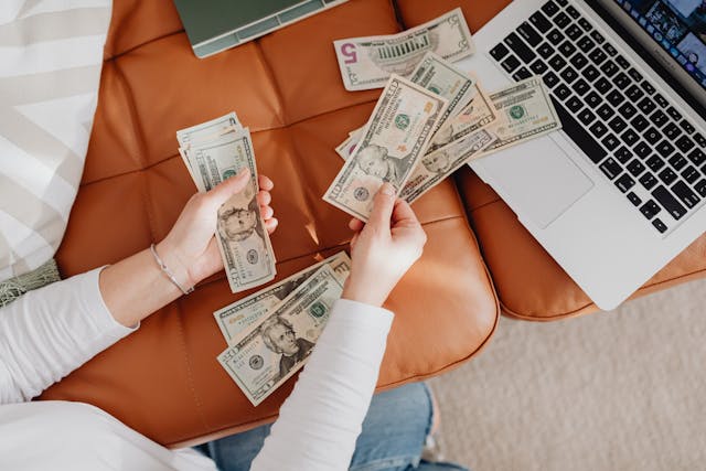A stack of dollar bills next to a laptop, symbolizing online earnings through Gumroad.