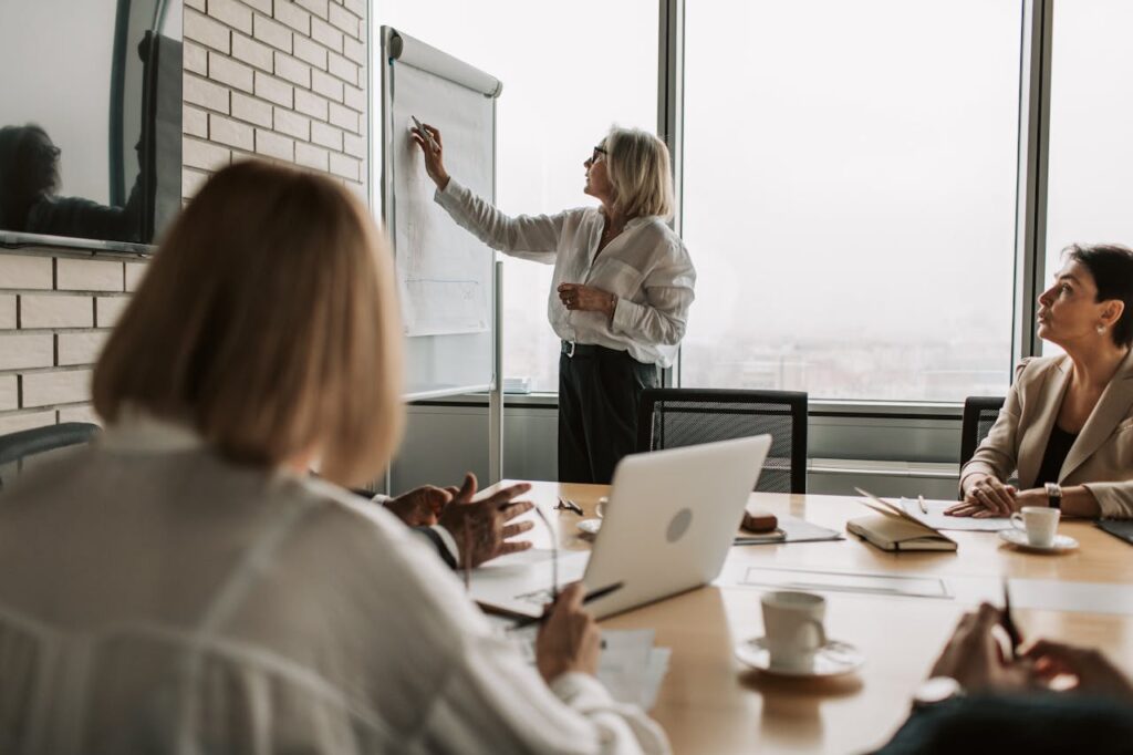A confident business leader presenting wealth-building strategies on a whiteboard to an engaged, diverse team, symbolizing transformative mindset examples.